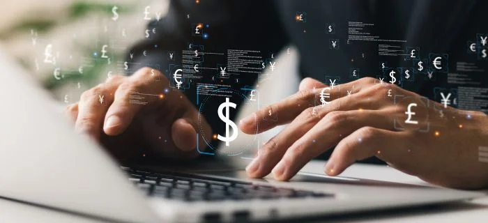 Close-up of hands typing on laptop keyboard with floating currency symbols and digital data.