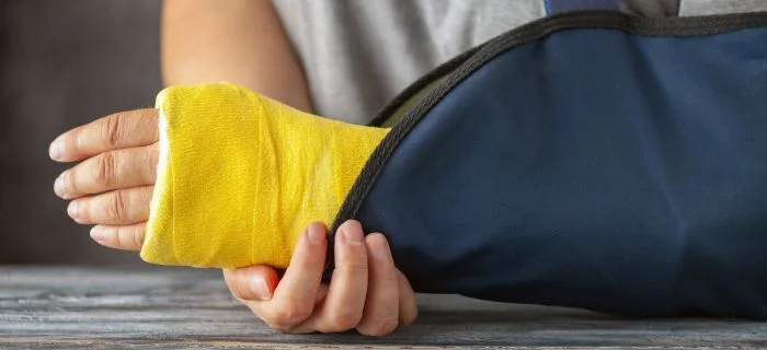 Person with yellow wrist cast supported by a blue arm sling on a gray surface.
