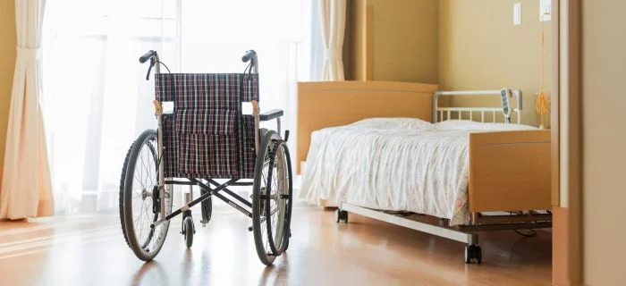 Empty black and red plaid wheelchair positioned near a hospital bed in a bright room.