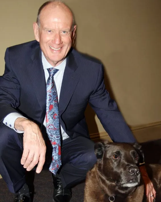 Man in navy suit with patterned tie crouching next to a brown dog indoors.