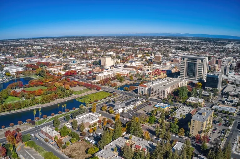 Aerial view of a cityscape with autumn foliage, waterways, and various commercial and residential buildings under a clear blue sky.
