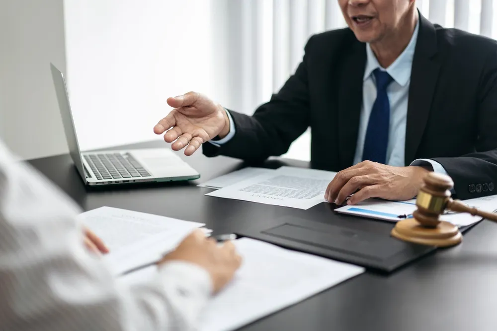 Professional male lawyer in black suit discussing documents with client at desk.