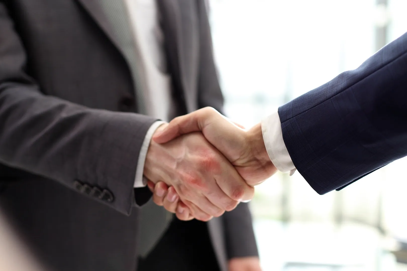 Two individuals in business suits shaking hands in a professional setting.