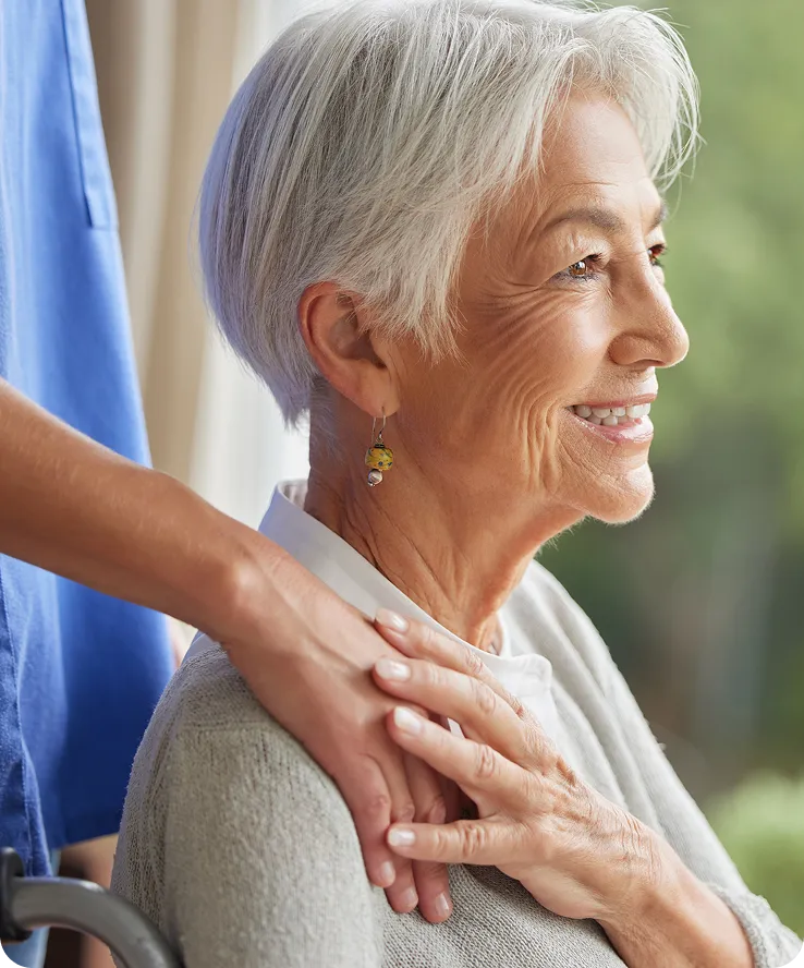 Elderly woman with short gray hair smiling, receiving comforting hand on shoulder.