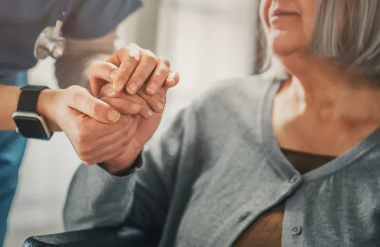 Healthcare professional holding elderly woman's hand, conveying support and care.
