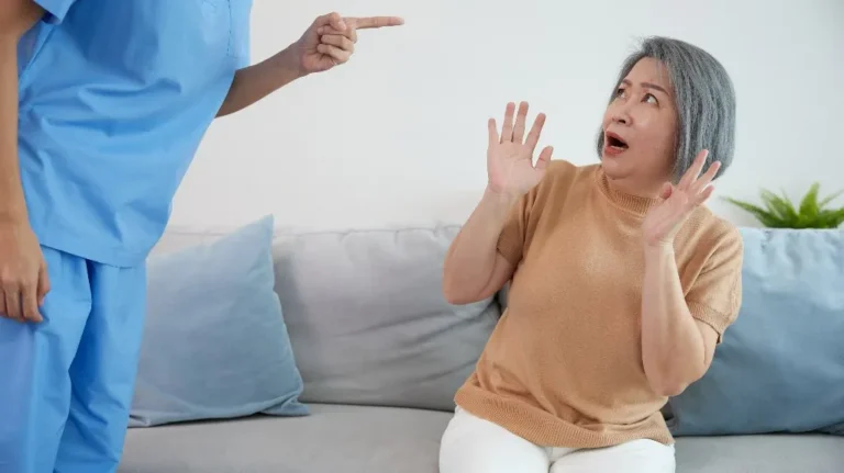 Healthcare professional in blue scrubs pointing, elderly woman in beige sweater reacting fearfully.