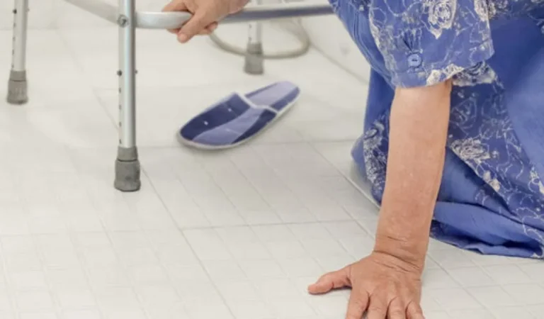 Elderly person in blue clothing fallen on tiled floor, holding walker for support.
