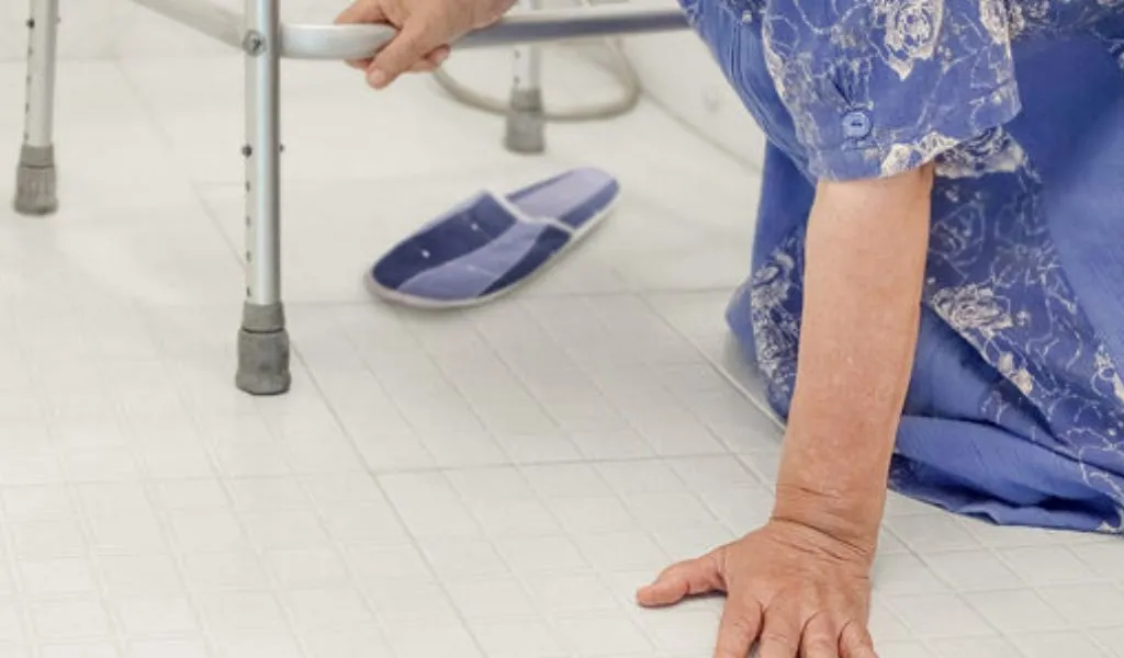 Elderly person in blue clothing fallen on tiled floor, holding walker for support.