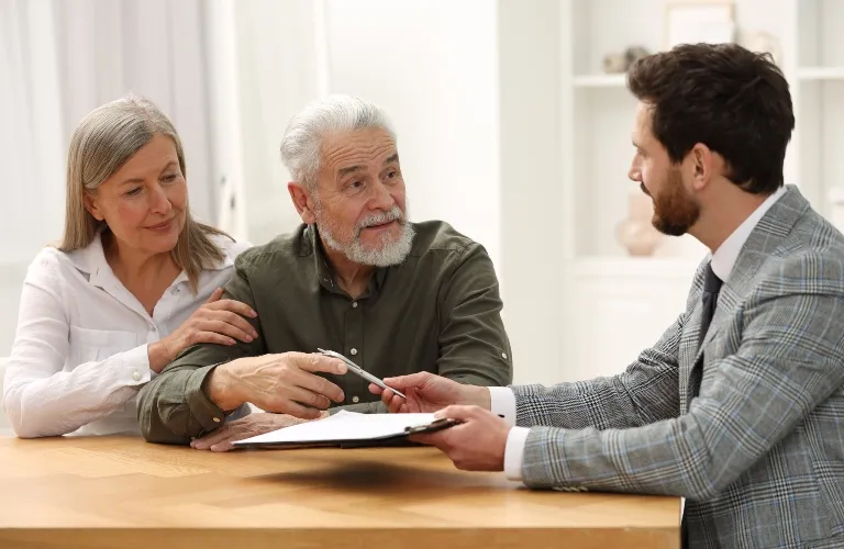 Older couple consulting with a professional man in a gray suit at a wooden table.