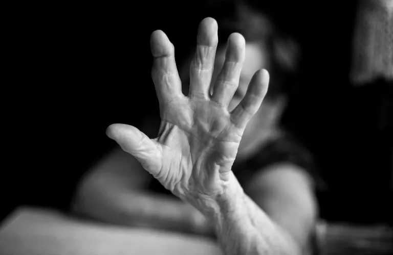 Black and white close-up of an outstretched elderly hand with blurred background.